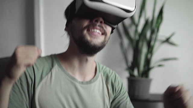 留着胡子的年轻潮男使用VR头盔显示器观看360度视频，感觉就像坐在家里客厅的沙发上听音乐会或跳迪斯科。虚拟现实技术。视频素材