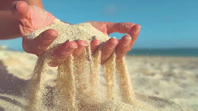 慢镜头:一名认不出来的女游客将沙子撒向岸边。视频素材