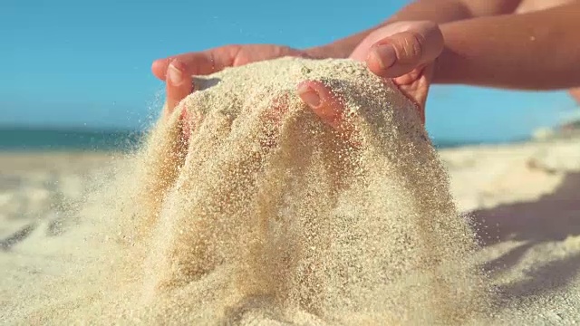 慢镜头:一个女人抓起一把沙子，用手指把它筛了一遍。视频素材