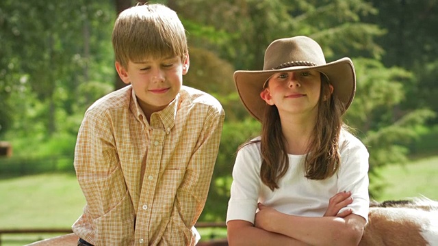 一个男孩和一个戴牛仔帽的女孩坐在木篱笆上视频下载