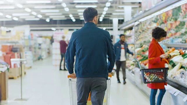 在超级市场:推着购物车的人通过商店的新鲜农产品区。商店与许多顾客购物。后面的视图拍摄。视频素材