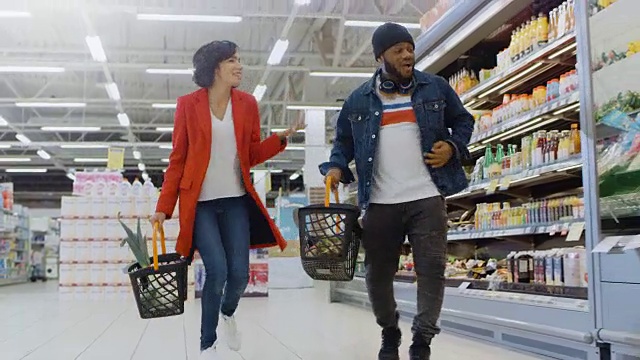 在超市:美丽快乐的夫妇带着购物篮在商店的新鲜农产品区跳舞。快乐的男人和女人在商店里快乐的跳舞，在购物的时候开心。视频素材