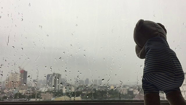 孤独的泰迪熊带着雨滴在窗前哭泣的画面。视频素材