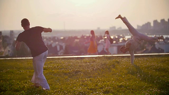 体格强健的男子在过往的人群和美丽的日落背景下跳卡波耶拉舞视频素材