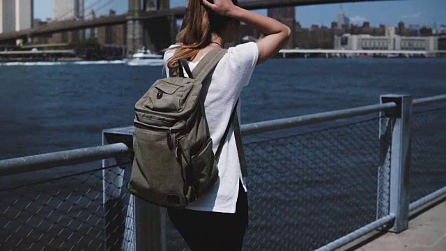 镜头跟随年轻女游客背包享受轻松漫步布鲁克林大桥在阳光明媚的河岸视频素材