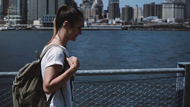快乐年轻美丽的女孩背包沿着纽约天际线全景，微笑着享受阳光明媚的早晨视频素材