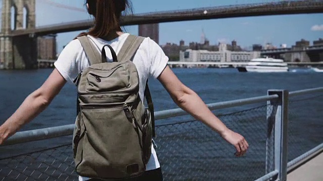美丽的年轻女游客背包举起双臂，在纽约曼哈顿天际线全景附近的喜悦视频素材
