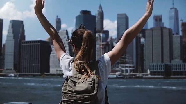 美丽的女性旅行者与背包举起双臂与兴奋曼哈顿城市天际线附近在纽约视频素材