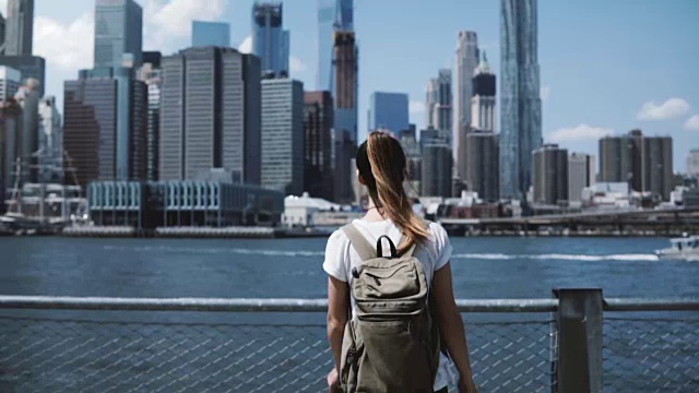 年轻快乐的旅游女孩背着背包，双臂张开，在纽约著名的曼哈顿天际线视频素材
