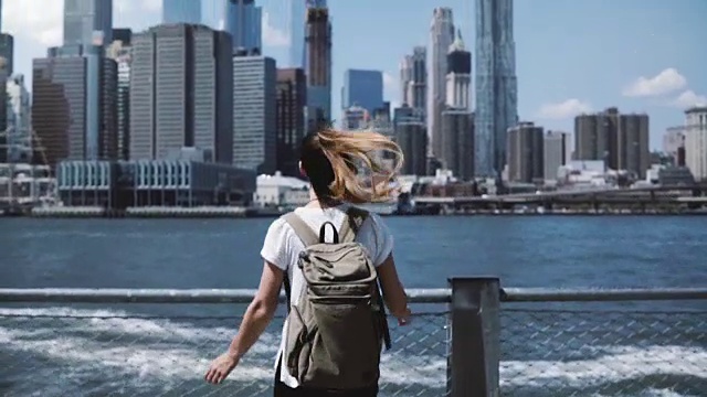 镜头跟随年轻快乐的旅行者女孩背着背包，张开双臂在纽约曼哈顿的天际线上跳跃视频素材