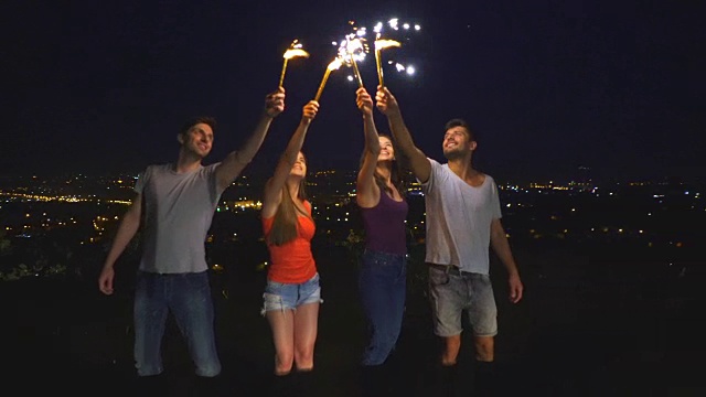 这四个人拿着烟花棒站在城市的背景上。晚上的时间视频素材