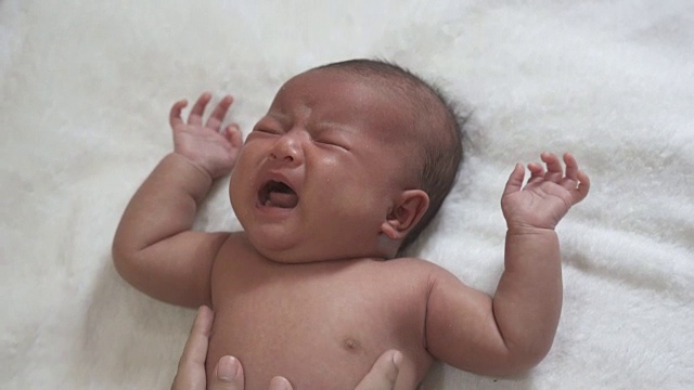 一个新生儿躺在白布上哭。视频下载
