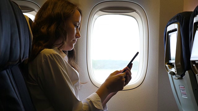 女商人在飞机上使用智能手机视频下载
