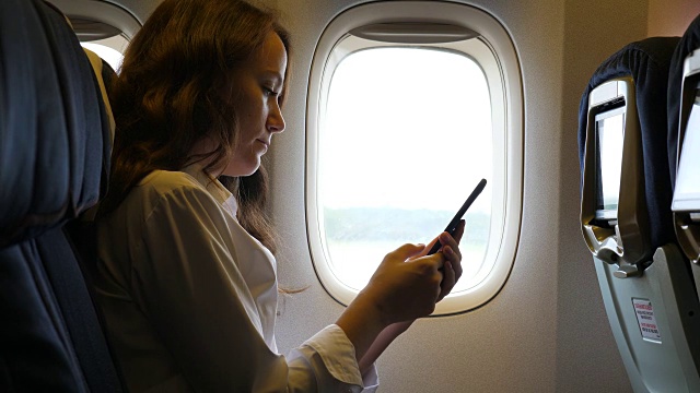 年轻女子在飞机上浏览智能手机视频下载