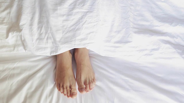 女性的腿在床上从上面看，白色床上用品，全高清视频素材