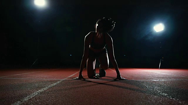 身材苗条的年轻女孩运动员正准备在跑道上的垫子上以慢动作开始跑步视频素材