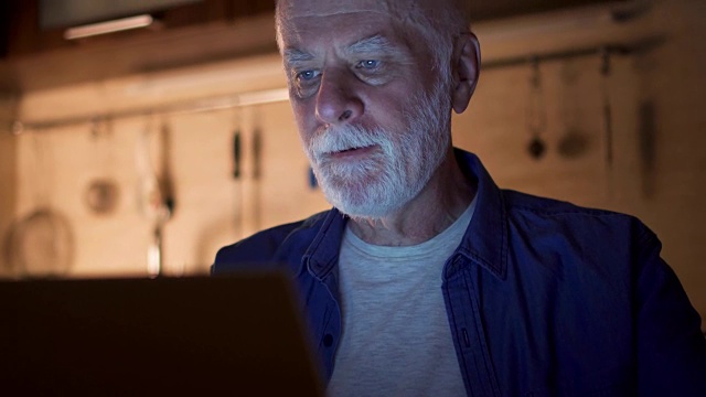 老人一边用笔记本电脑一边喝咖啡。晚上在家办公的自由职业者视频素材