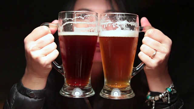 一个愚蠢的女人拿着生啤酒庆祝，拿着两个大杯子为自己祝酒。拿着淡啤对着镜头傻乎乎的女孩。视频素材