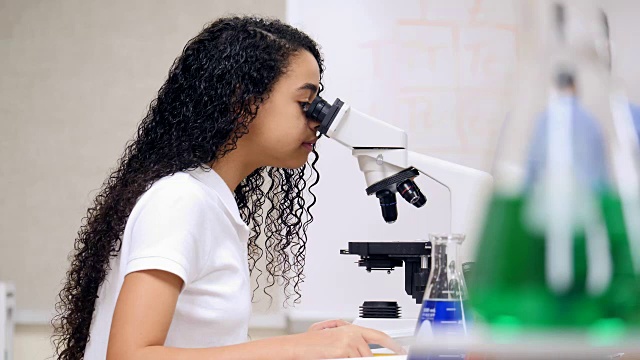 女子中学集中精力分析显微镜载玻片上的东西视频素材