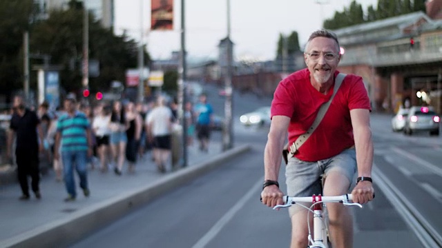 60多岁的老人活跃、运动、健康，留着灰白的短发和灰白的胡须，夏天他喜欢城市生活方式，穿着短裤和红色t恤，骑着时髦的单速城市自行车。视频下载