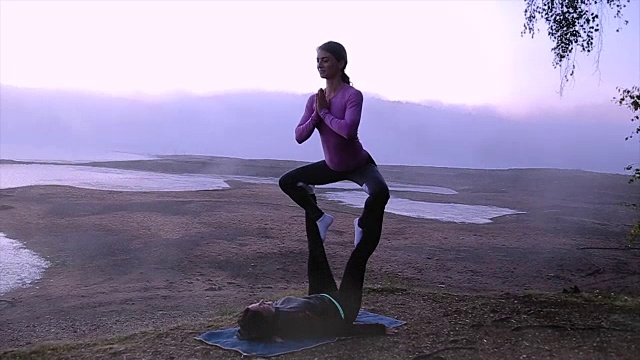 两个女孩在一个美丽的雾蒙蒙的湖边练习瑜伽视频素材