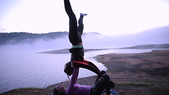 在瑜伽课上，两名运动爱好者结伴练习瑜伽，情侣在雾蒙蒙的湖边做伸展运动视频素材
