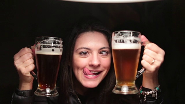 女人拿着生啤酒庆祝，拿着两个大杯子为自己干杯。女孩拿着淡啤对着镜头祝酒视频素材