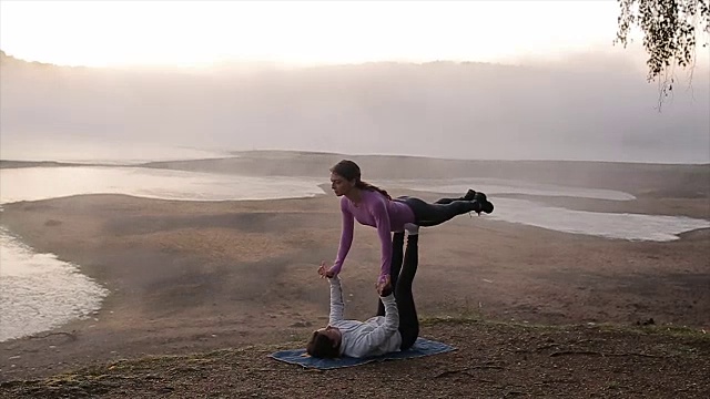 日出时分，两个女性朋友在美丽的雾蒙蒙的湖边练习瑜伽视频素材