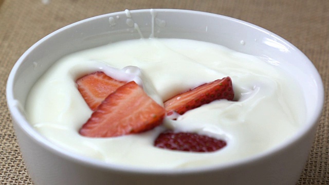 慢镜头里，草莓掉到酸奶里溅起水花。早上的早餐。视频素材