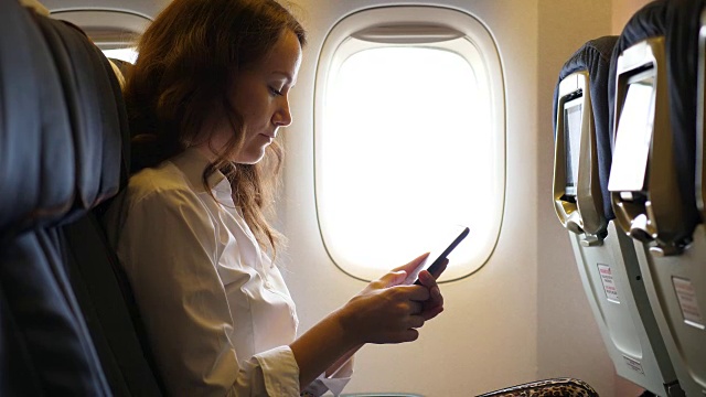 年轻女子在飞机上用智能手机发短信视频下载