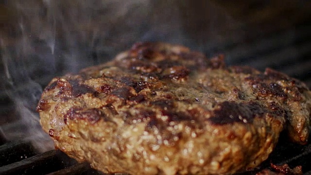 慢动作的牛肉汉堡在烧烤在近距离与火焰和烟雾视频素材
