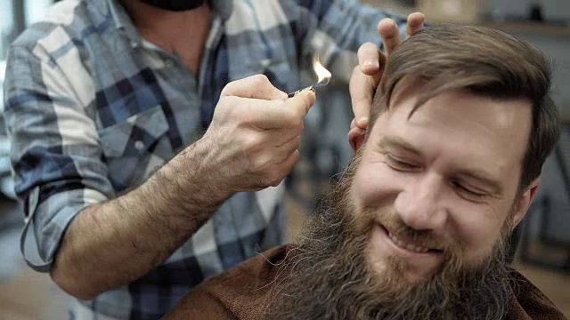 理发师在男子发廊里用火对留长胡子的成年男子。梳理胡子。工作场所的理发师。在理发店做胡子和理发。视频下载