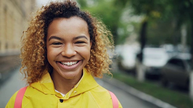 特写慢动作肖像好看的非洲裔美国妇女看镜头与高兴的微笑和大笑表达积极的情绪站在外面。视频素材