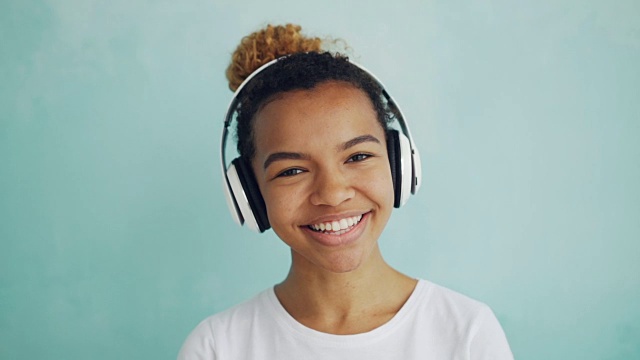 特写慢动作肖像快乐的非洲裔美国女孩戴着耳机看着相机，微笑和大笑。人，现代科技和乐趣的概念。视频素材