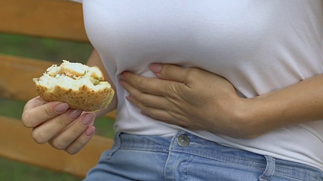 女人吃汉堡时，突然感到上腹疼痛，胃炎，吃垃圾食品视频素材