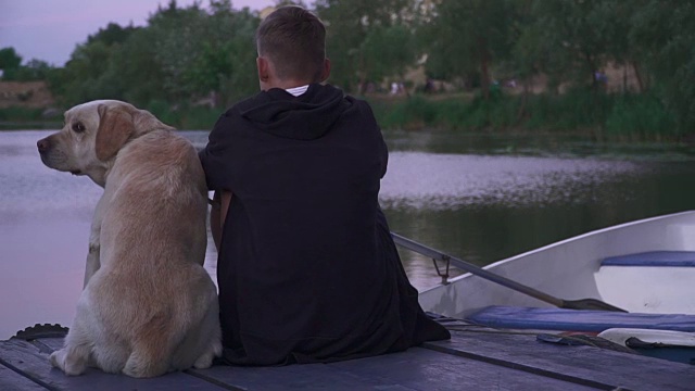 一个年轻人带着一只狗在湖边的码头上视频素材