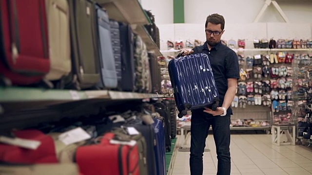 一名男性购物者正从超市的货架上拿起塑料手提箱，仔细检查视频素材