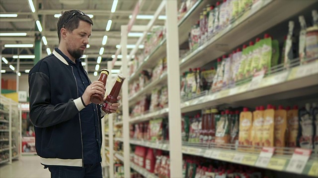超市的男顾客正在用番茄酱比较两瓶视频素材