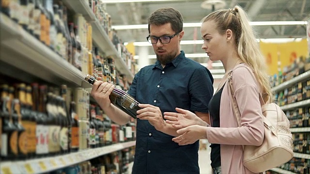 年轻的女孩和男孩正在超市的大厅里检查一瓶啤酒视频素材