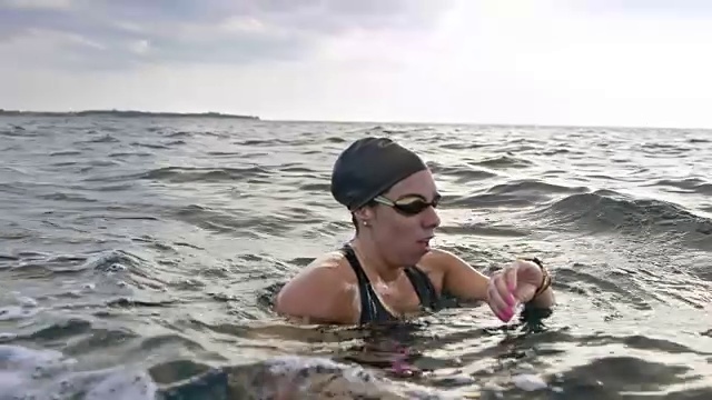 SLO MO女性开放水域游泳运动员停止在水和检查她的手表视频素材