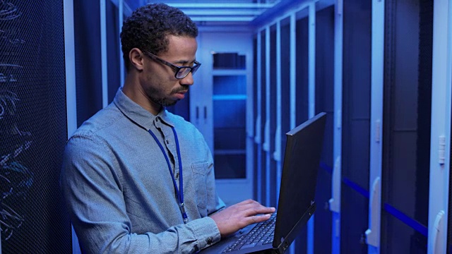 一个男性网络工程师拿着笔记本电脑站在服务器室做系统检查视频下载