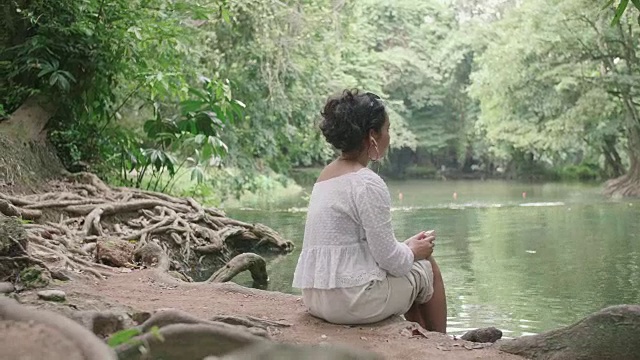 年轻的女性坐在瀑布边听音乐。视频素材
