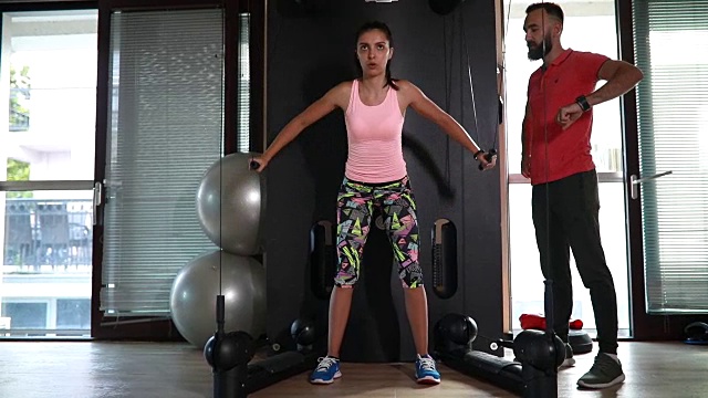 一个年轻女子在健身房和私人教练锻炼视频素材