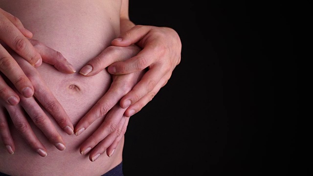 夫妇在怀孕的肚子上制作心形与他们的手近距离4K视频素材