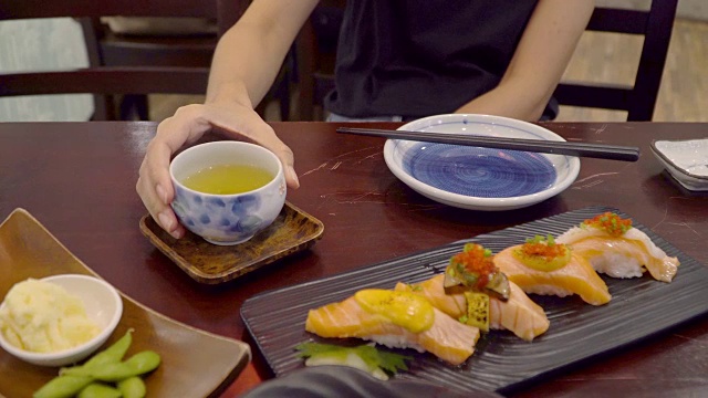 亚洲妇女喜欢吃日本寿司和绿茶在午餐时间在日本餐厅视频素材