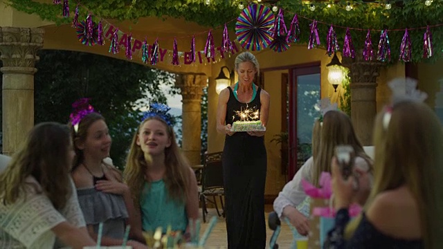 在美国犹他州雪松山的生日派对上，一名妇女拿着带有烟花的蛋糕给女孩们视频素材
