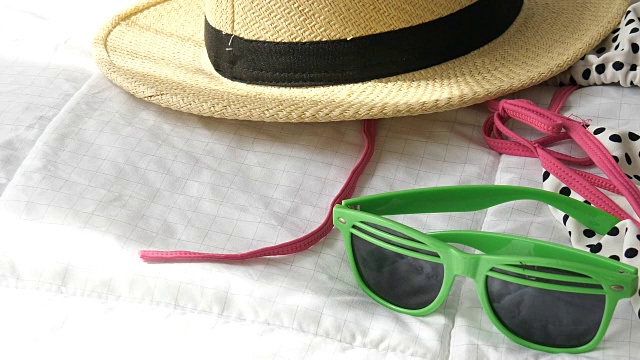 草帽，绿色太阳眼镜和比基尼在白色的床上，准备背包和假期。视频素材
