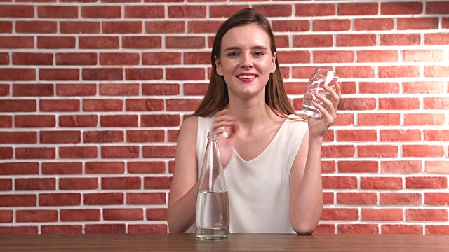 一个年轻漂亮的女人从玻璃杯里喝水视频素材