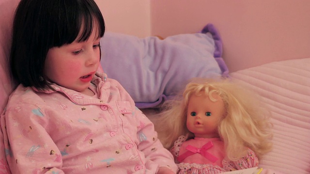 女孩在床上对着洋娃娃读书视频素材
