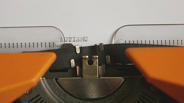 一个人用声音在一台旧打字机上写AUTISMUS的特写镜头视频素材